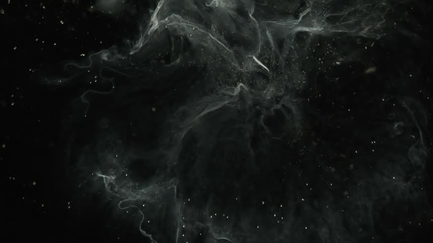 Strands and dots of white floating ink slowly moving over a dark background