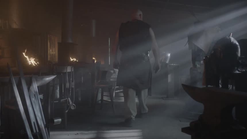 A large man walks past burning fires inside a room