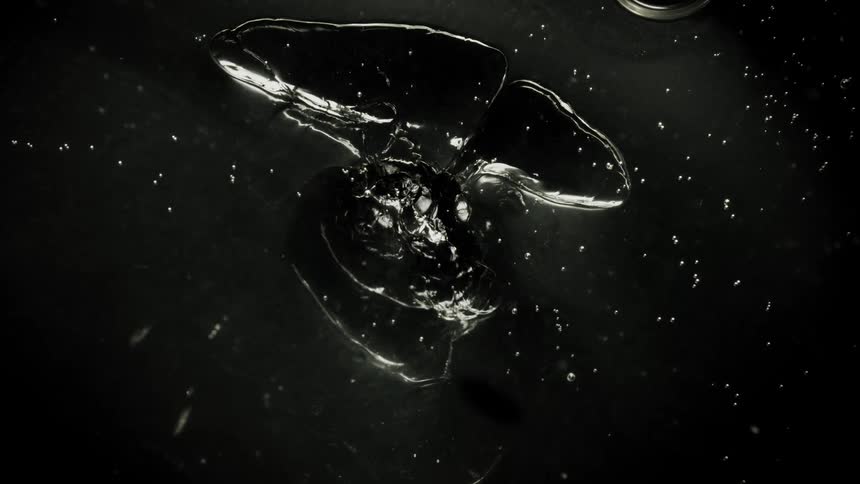 A clear liquid substance is shapeshifting and moving in the darkness among floating spheres