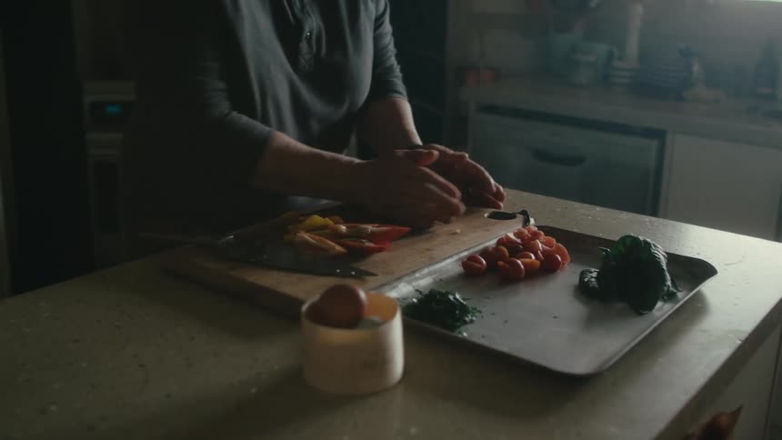 A person uses a knife to chop food on a cutting board before scooping up the food with their hands and carrying it to the sink
