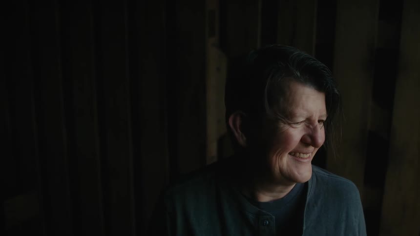 Middle aged woman smiles outdoors near rough wooden ball