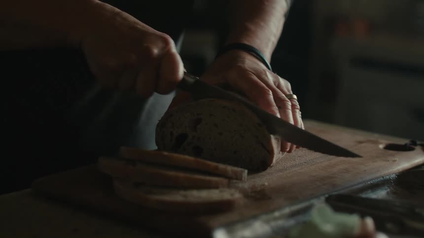 A person cutting a loaf of bread on a wooden cutting board
