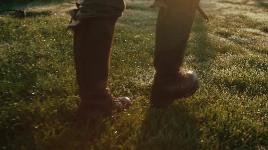 A person in rubber boots walking over a grassy lawn