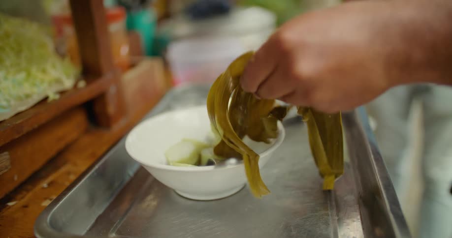 A person cutting produce into a white bowl on a metal tray