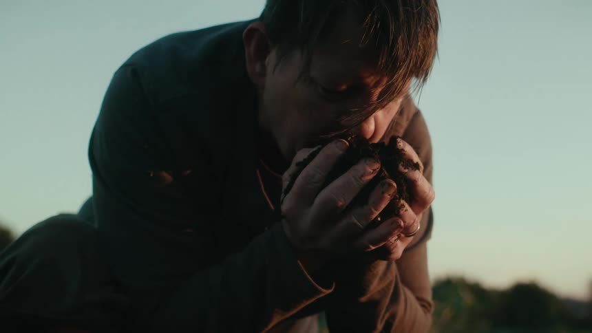 Farmer smells a clump of dark brown loam he picked up with his hands at morning