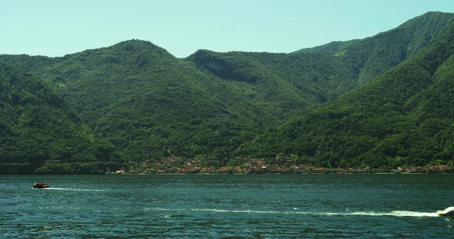 Boats moving over the calm surface of a lake close to a waterfront town in the mountains