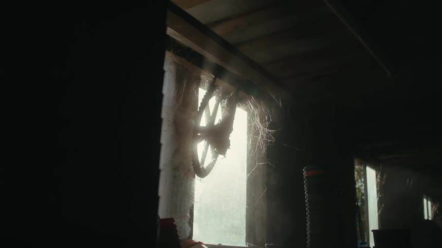 Metallic wheel gear hanging from the window of a barn covered in cobwebs at morning