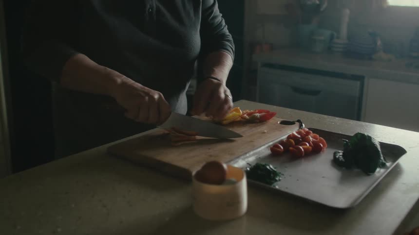 Woman with sweatshirt cuts vegetables on cutting board in the kitchen