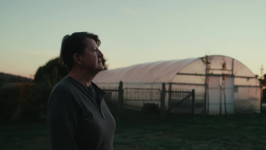 A woman is standing outside near a greenhouse