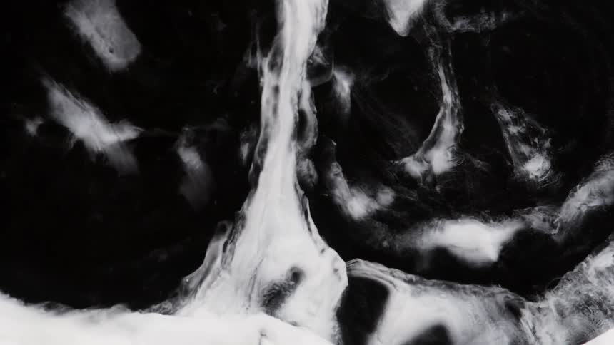 A white substance spreads out in a dark area but then the black pushes away the white
