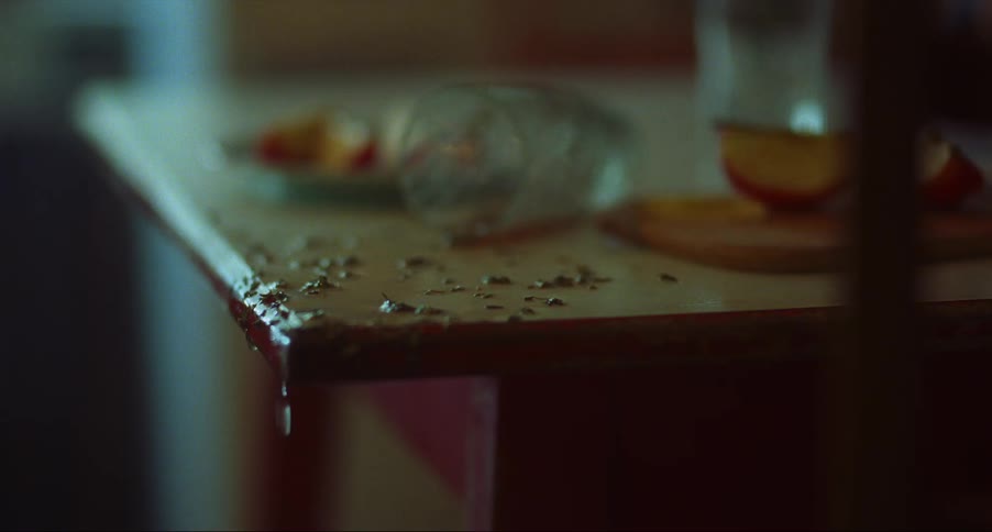 Spilled juice from a glass over a table dripping on the floor of a dimly lit room