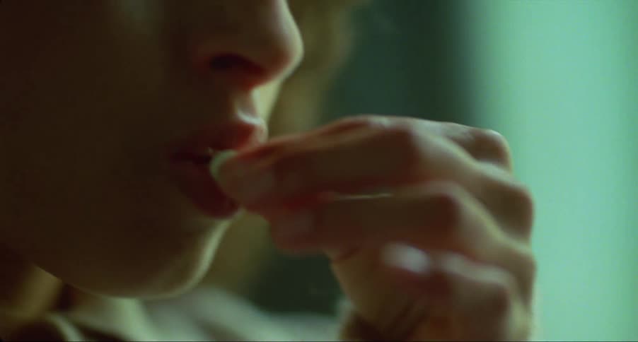 A woman is standing in a room and she takes a pill out of the plastic pack and puts it in her mouth
