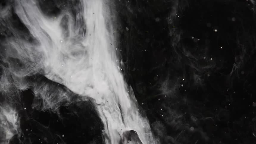 Strands and dots of white floating ink slowly moving over a dark background