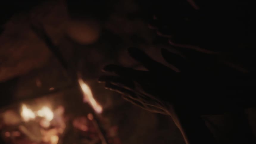 People warm themselves by a fire at night