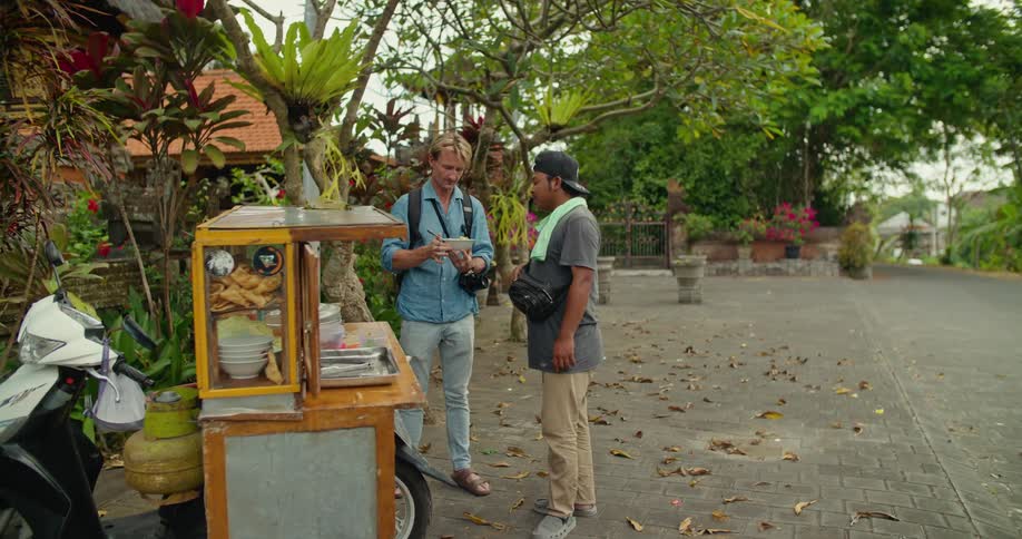 A food cart vendor describes the food in a bowl to a customer as they talk and smile