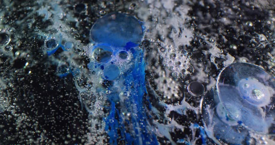 Bubbles are floating in a dark area with foam and a blue substance is blending in