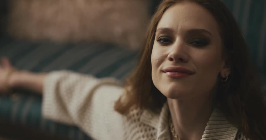 Woman with brown hair and white sweater sits on floor dancing in front of blue couch in the living room