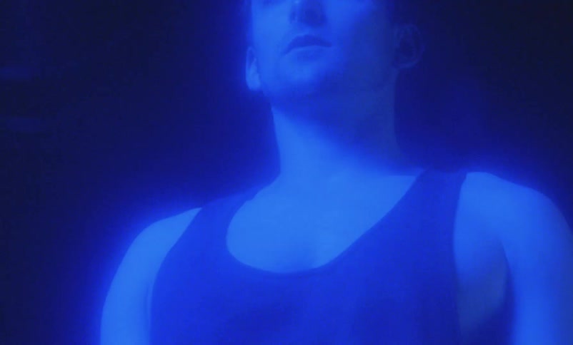 Angry and muscular man wearing undershirt screams with rage in purple light