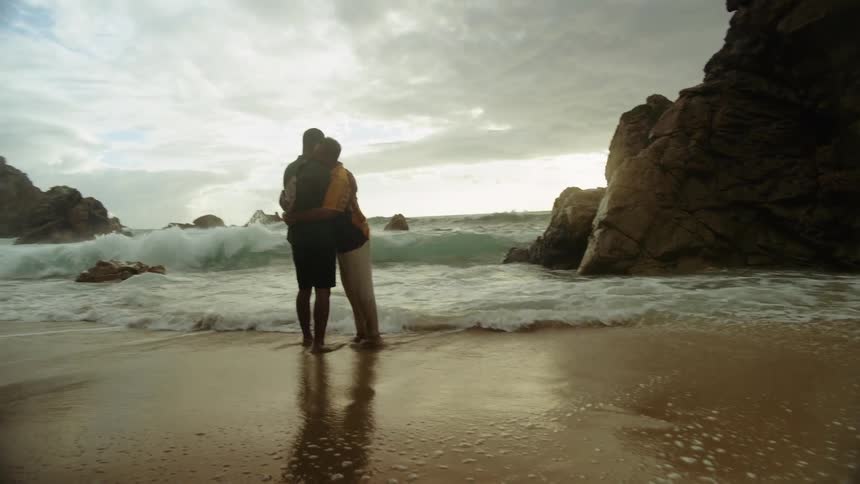 Two men hugging and kissing as they dodge the waves on wet sand