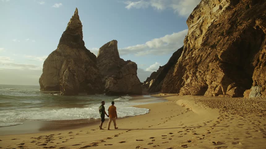 Two men holding hands while taking a stroll on a sandy beach
