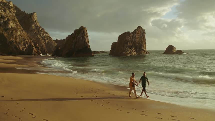 Couple walk holding hand on the wet sand close to the ocean at sunset