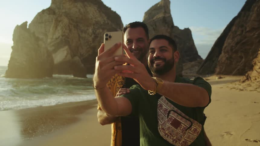 Two men taking a selfie picture close to the ocean at the beach