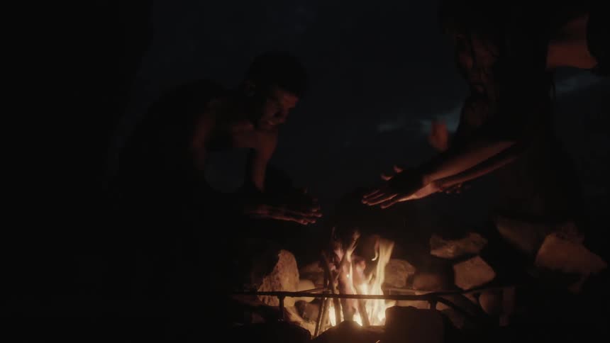 Two people warm their hands on a fire at night