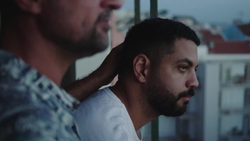 A man rubs his partners head while they stand on their balcony