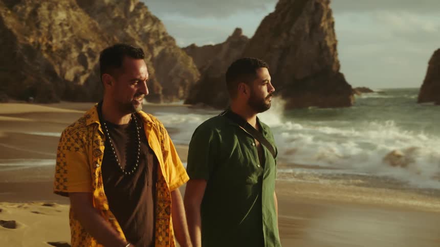 Two men holding hands while taking a stroll on a sandy beach