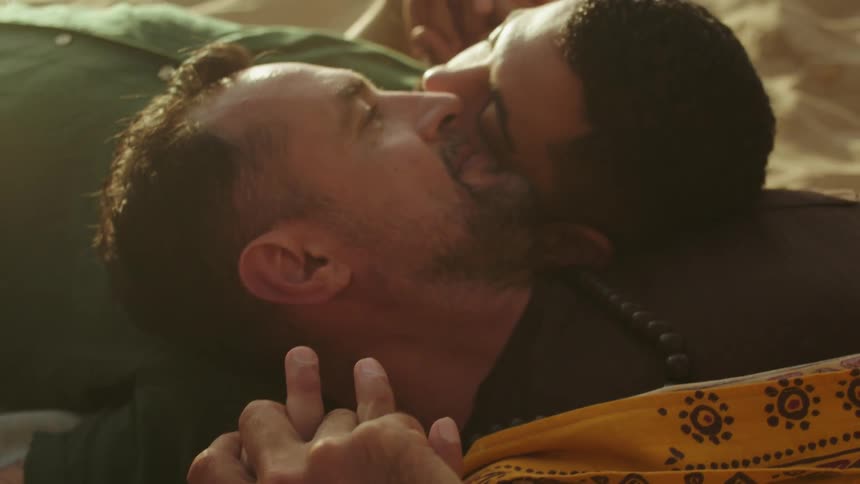 A couple lie on the beach with the heads on each others shoulders and hold hands