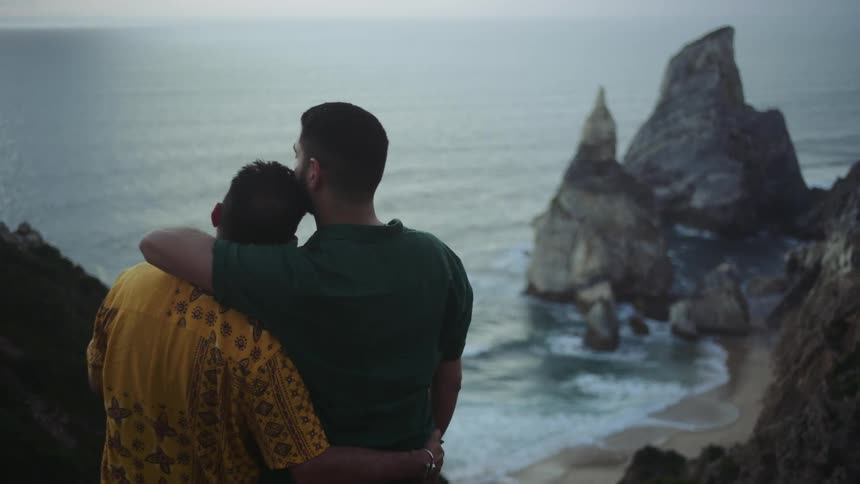 Young couple hug while looking at the ocean from a cliff near the coast