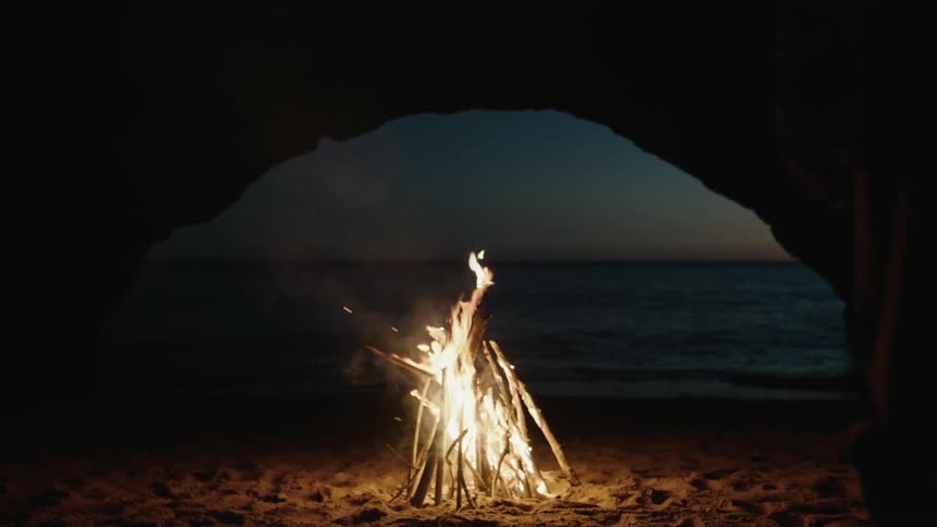 A fire burning in a beachside cave at night