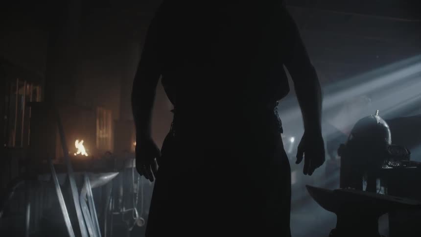 A man stands in a dark room where a small fire is burning