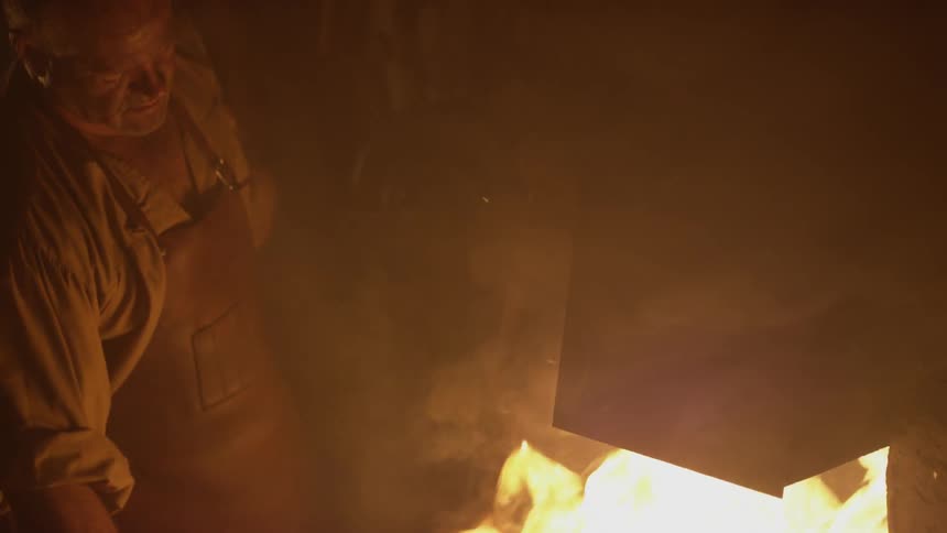 A man is stirring a fire in a blacksmith shop