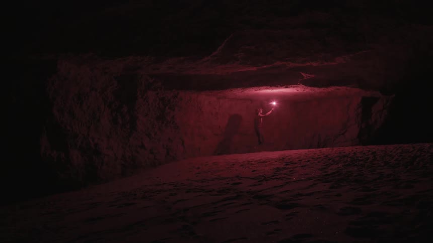 A man using a flare to explore a rock formation at night