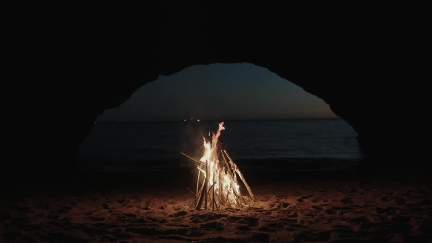 A fire is burning in a cave by the shore