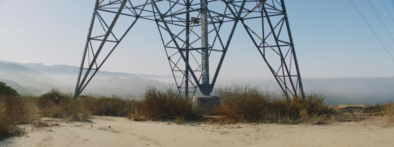 Close up of the bottom of a utility tower with hills in the distance