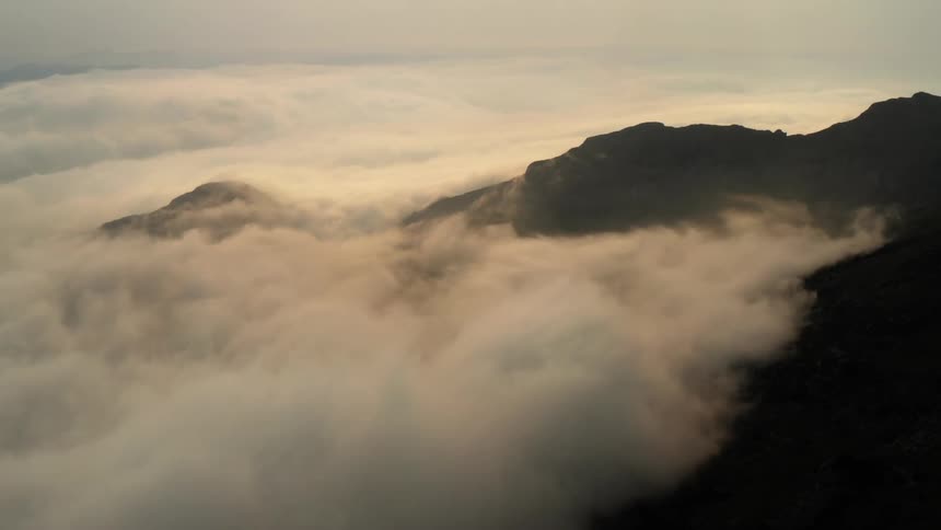 The top of a Spanish mountain ridge peaks through the clouds in pastel lighting