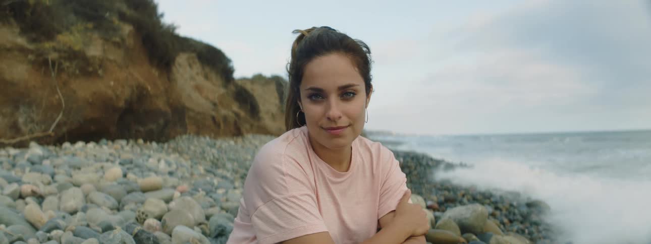 Young woman crouching over the rocks on a beach in the coast smiles at the camera