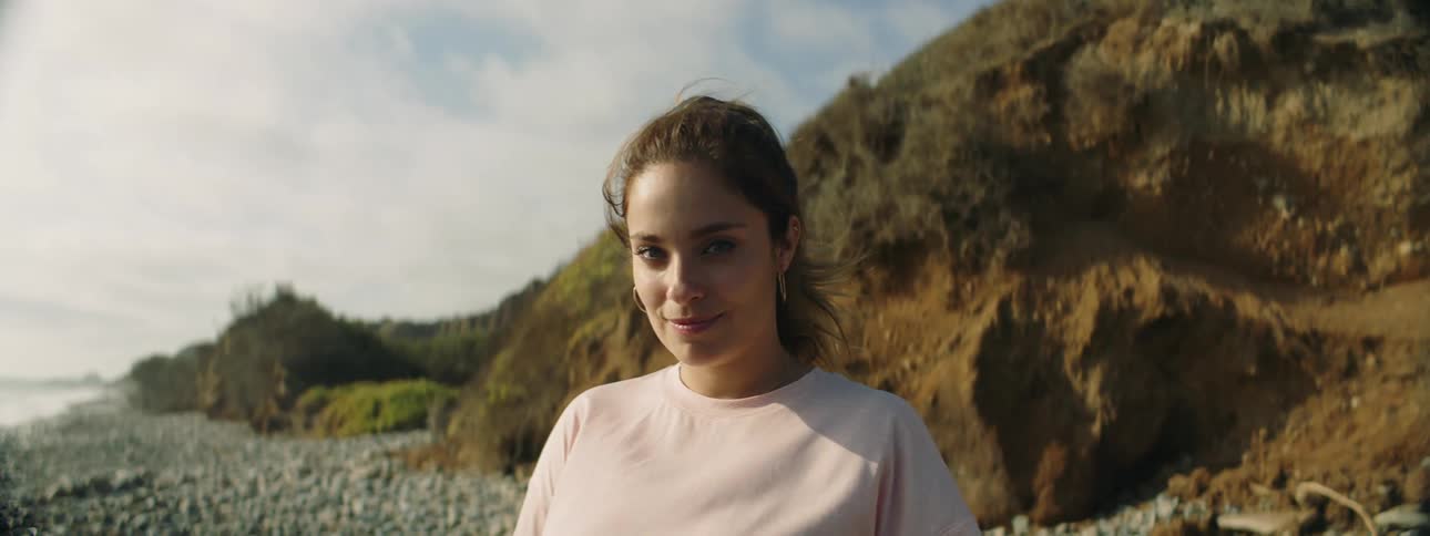 A woman smiles and closes her eyes as she stands on a beach