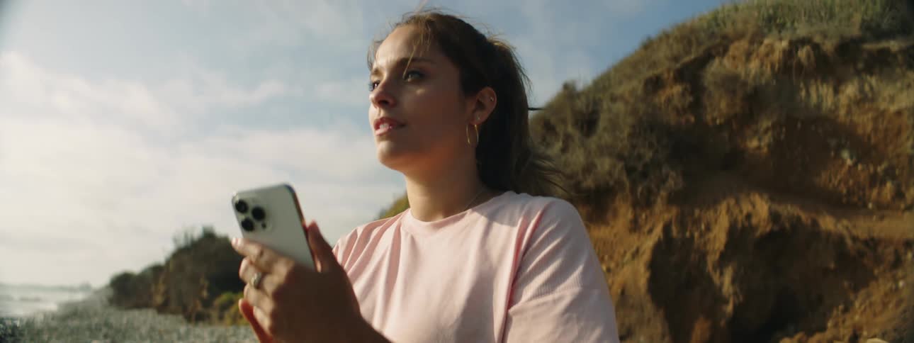 Young woman standing on a beach takes pictures of the coast and the ocean