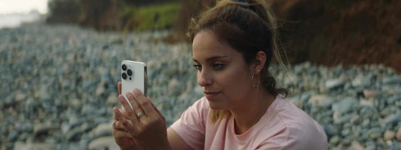 A woman sits on the beach and looks at her cell phone and smiles