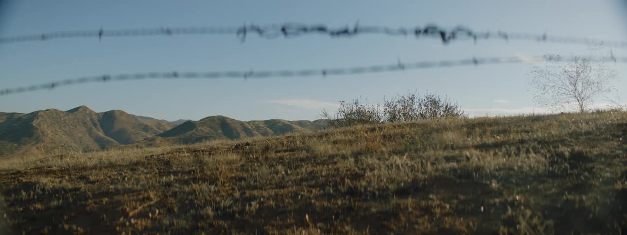 Mountains under a clear sky are seen through a barbed wire fence