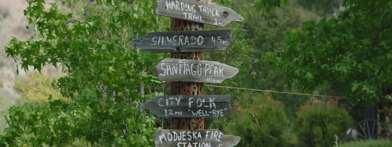 A pole is outside of the woods with signs directing people which way to go for each path