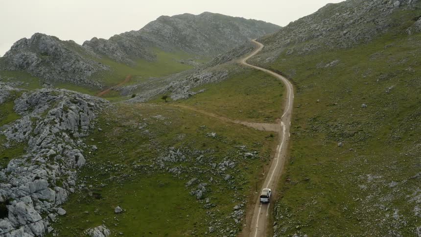 Aerial view of a car driving on a road on the gentle slopes of a mountain range at evening