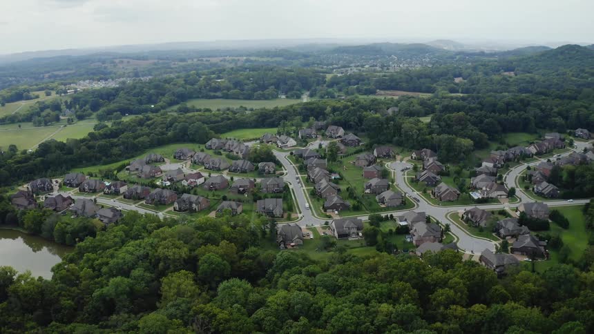 Aerial view of houses and roads in a community surrounded by trees and a nearby lake with mountains on the horizon