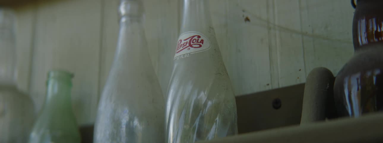 Empty vintage coca cola bottles over a wooden shelf covered in cobwebs