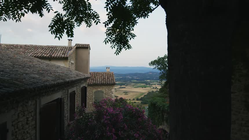 A brick building is near trees and plants overlooking the coast under a cloudy sky