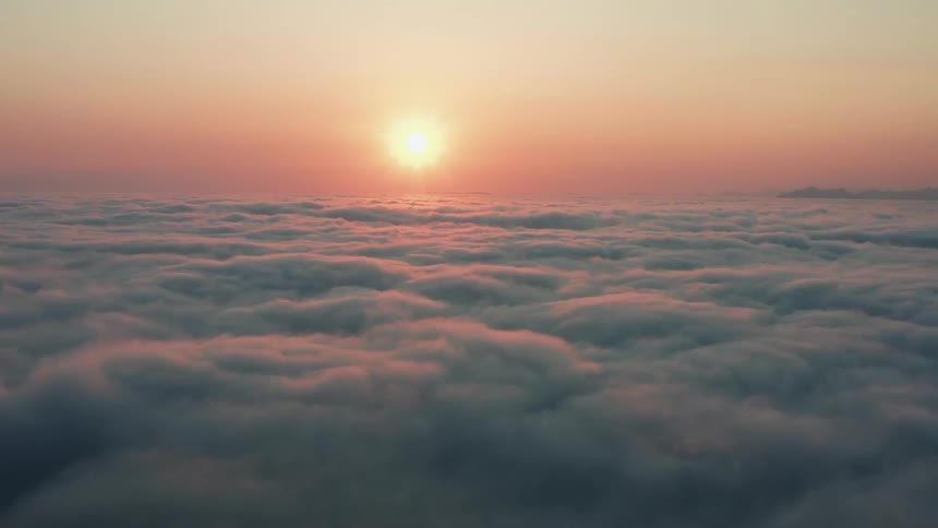 An aerial view of the sun setting over clouds in the sky