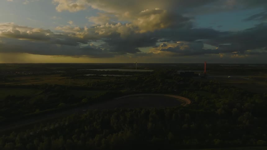 Clouds over a field with a river and a wind turbine